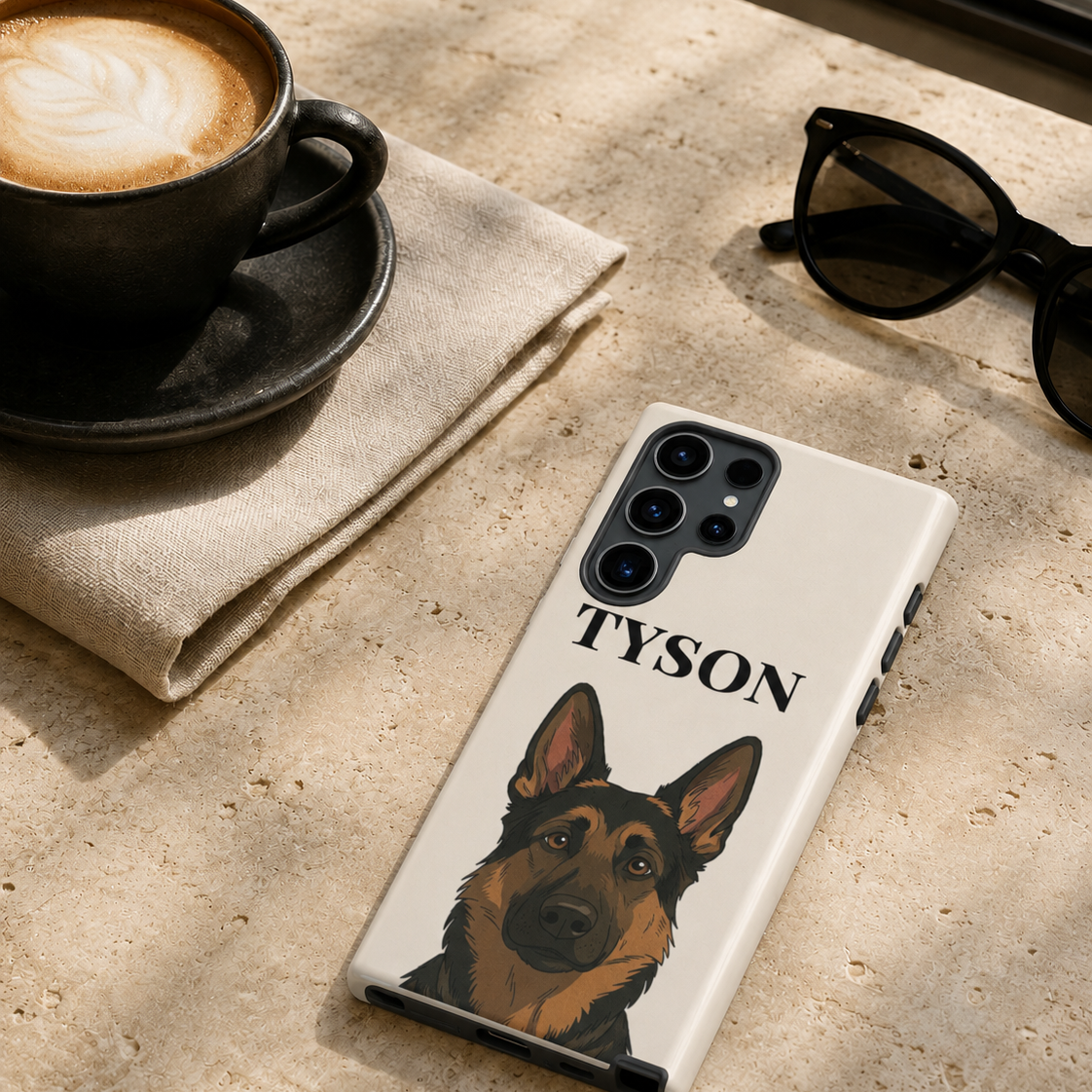 A white phone case featuring a custom German Shepherd illustration and the name 'TYSON' printed in black, displayed on a textured stone surface next to a cup of coffee and sunglasses.